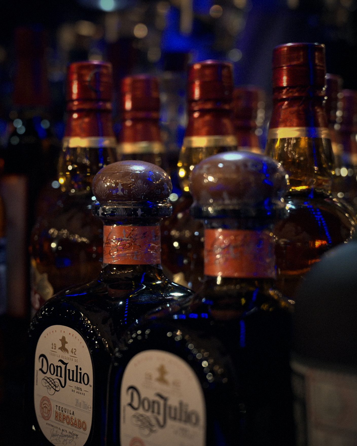 Tequila and whisky bottles on the blue-lit back bar