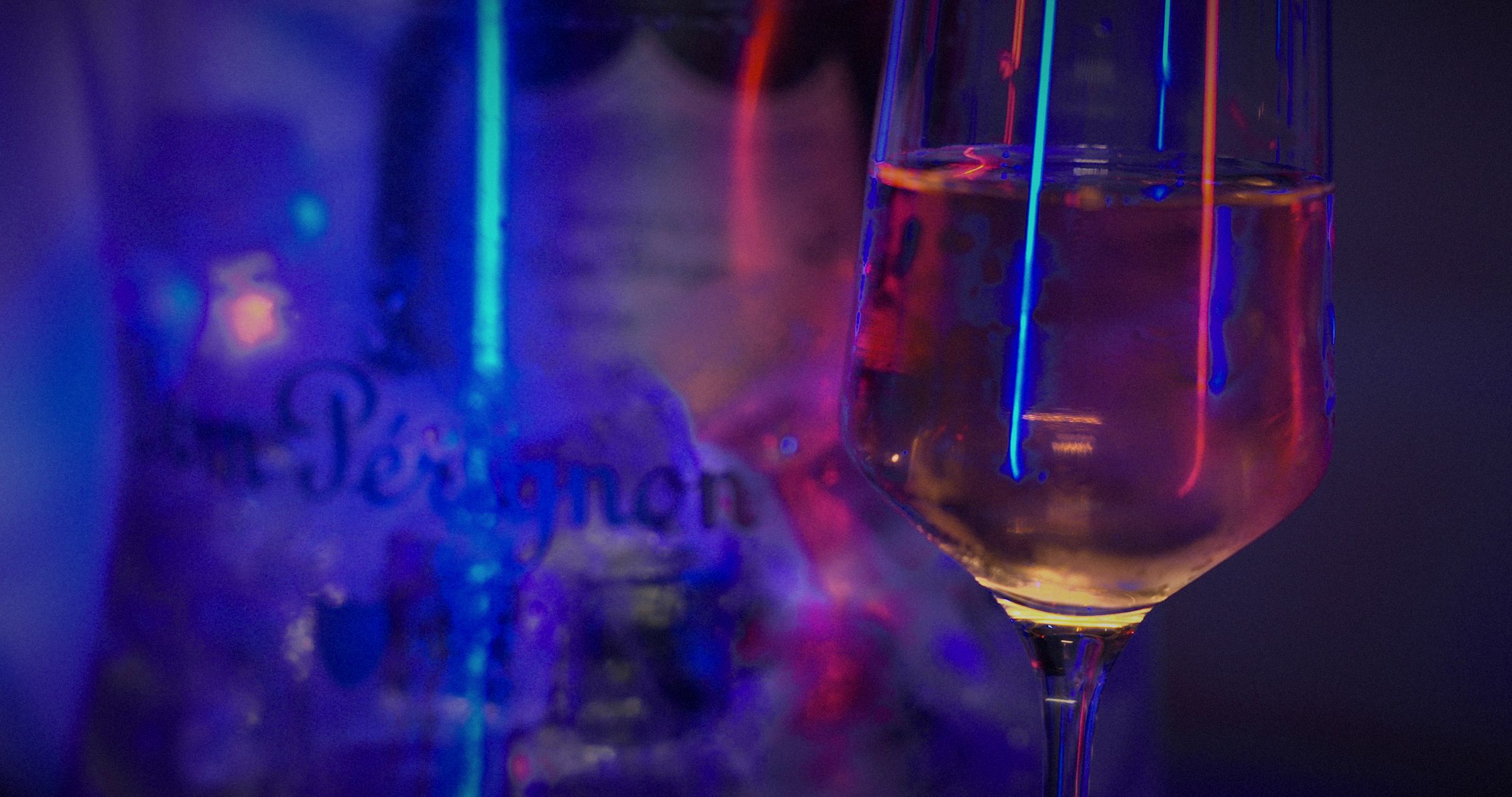 A glass of champagne beside a Dom Pérignon ice bucket in neon light