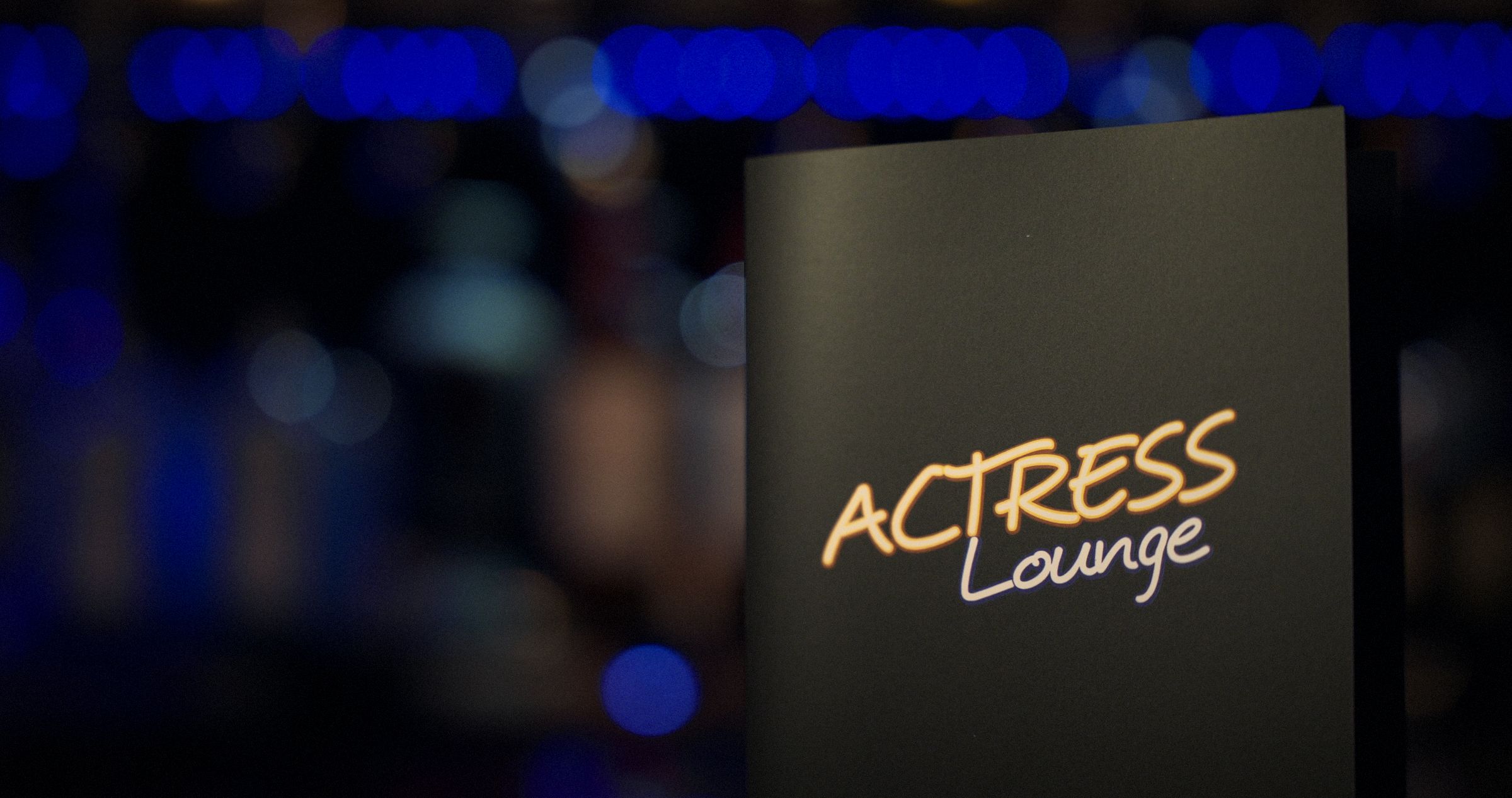 The Actress Lounge menu standing on the bar against blue-lit bottles